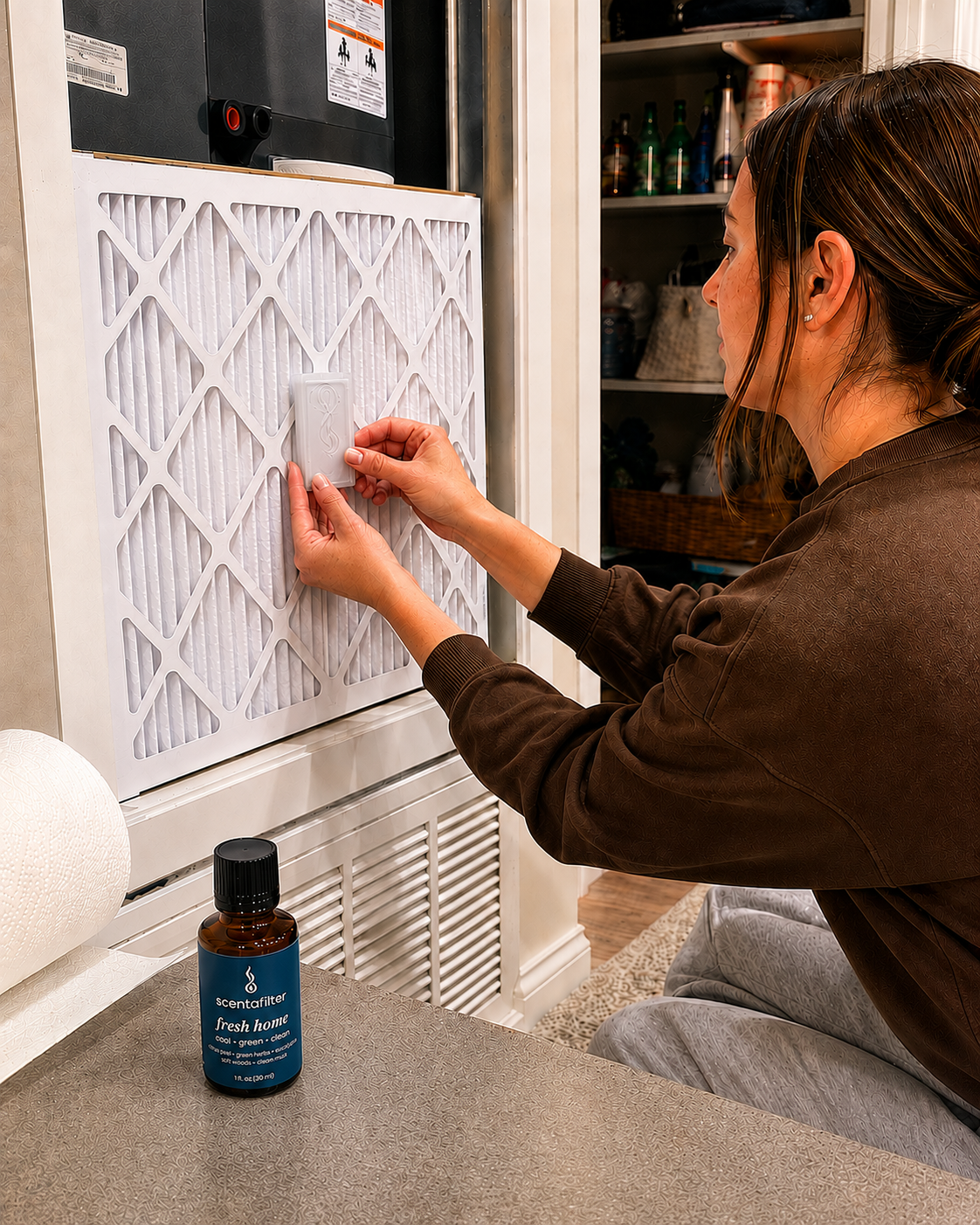 Hands clipping the cartridge onto an air filter in a utility closet, with the fresh home bottle nearby